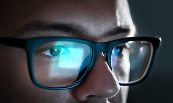 Close up of a man's eyes, a computer screen reflected in his glasses.