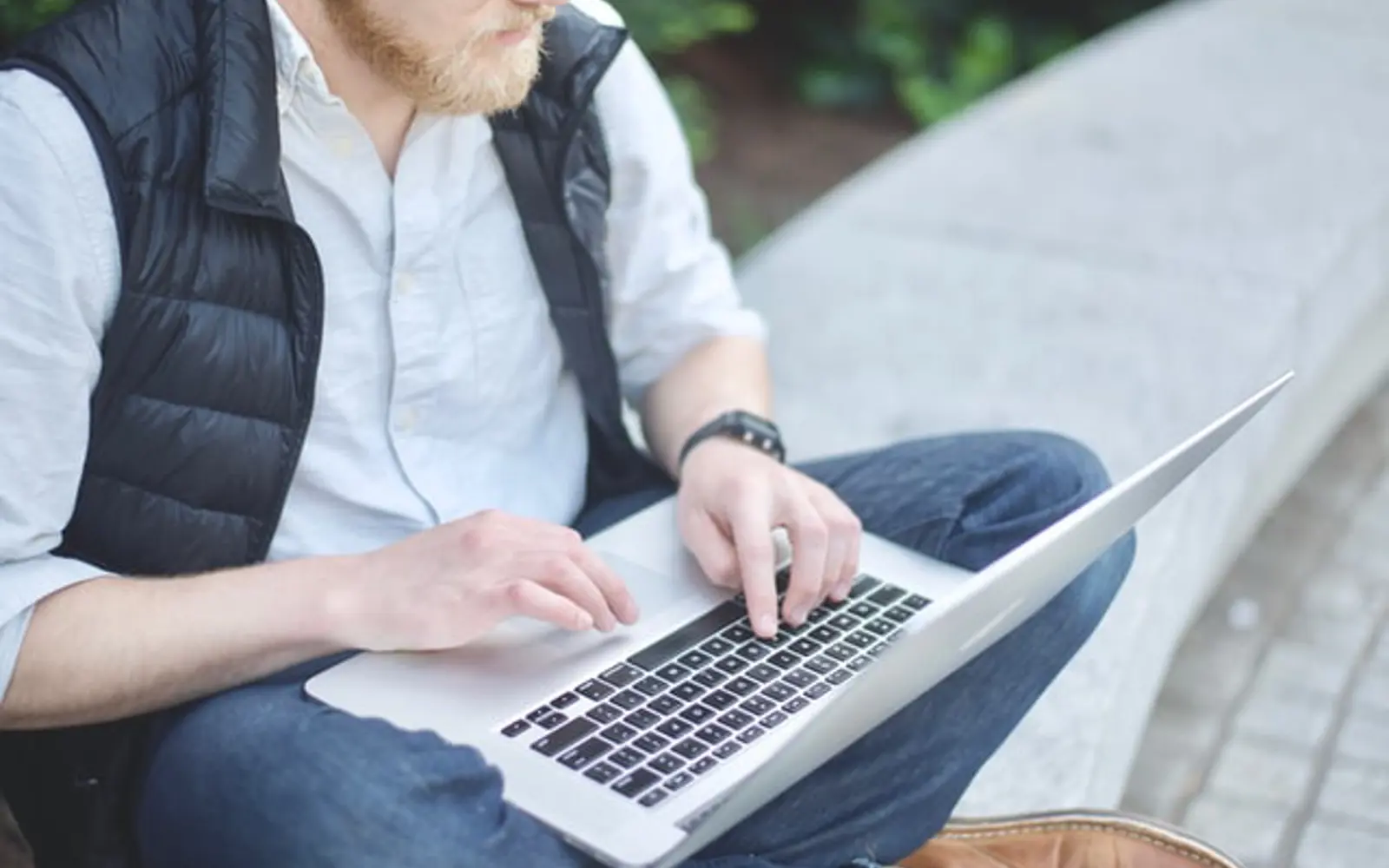 a man sitting on a stone bench using a laptop