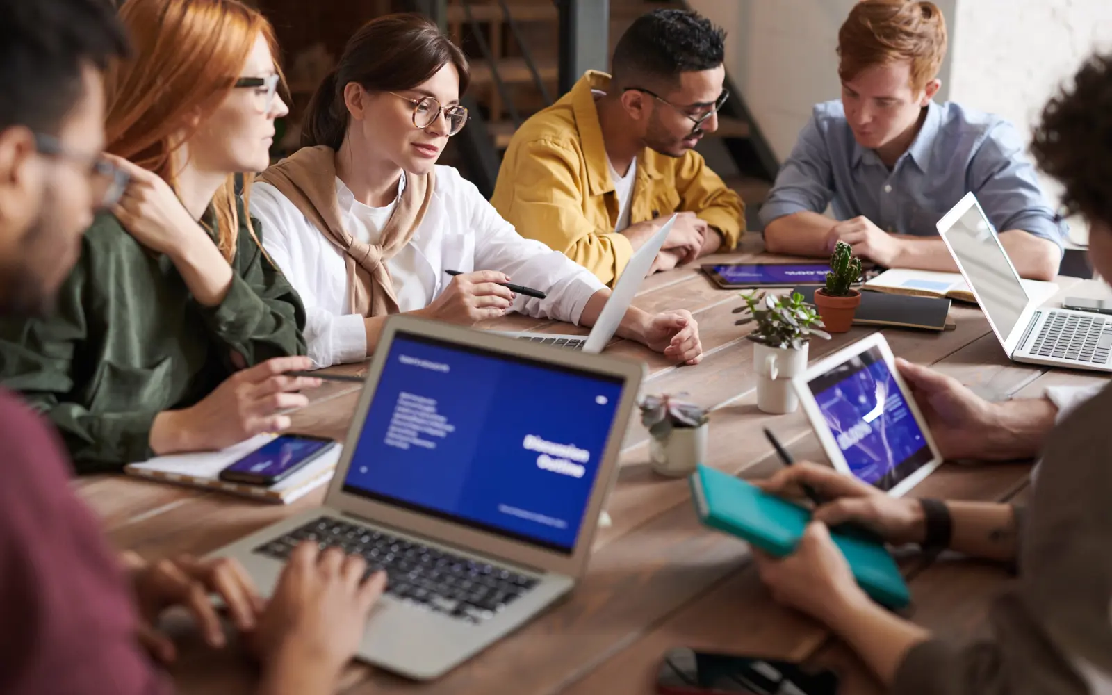 a group of people sitting around a table with laptops