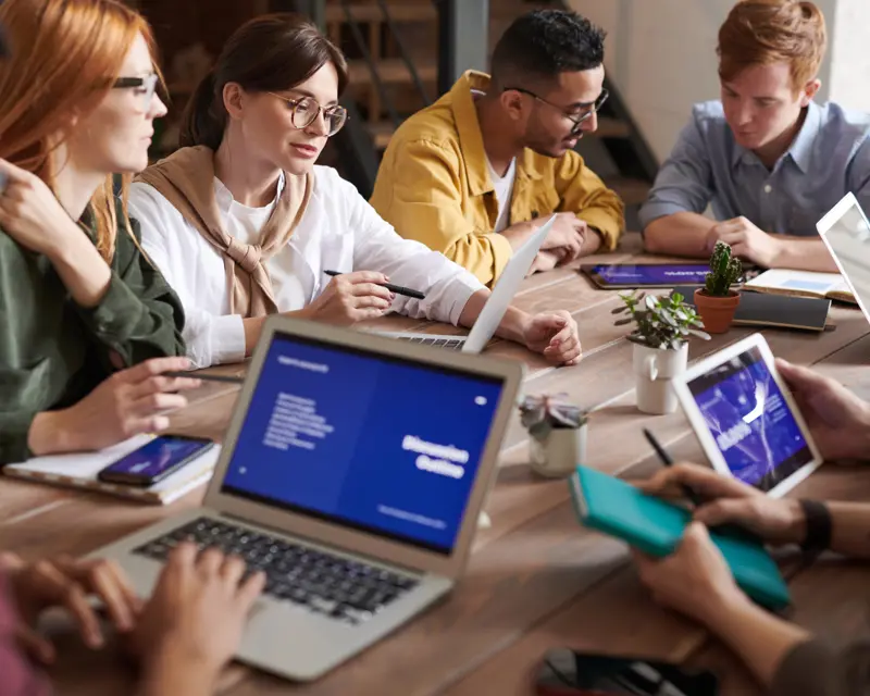 a group of people sitting around a table with laptops