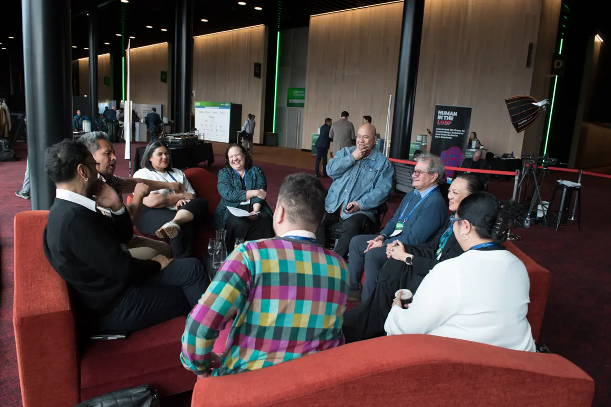 A group of attendees seated in a circle on red couches, laughing in conversation between sessions at the Aotearoa AI Summit 2026.