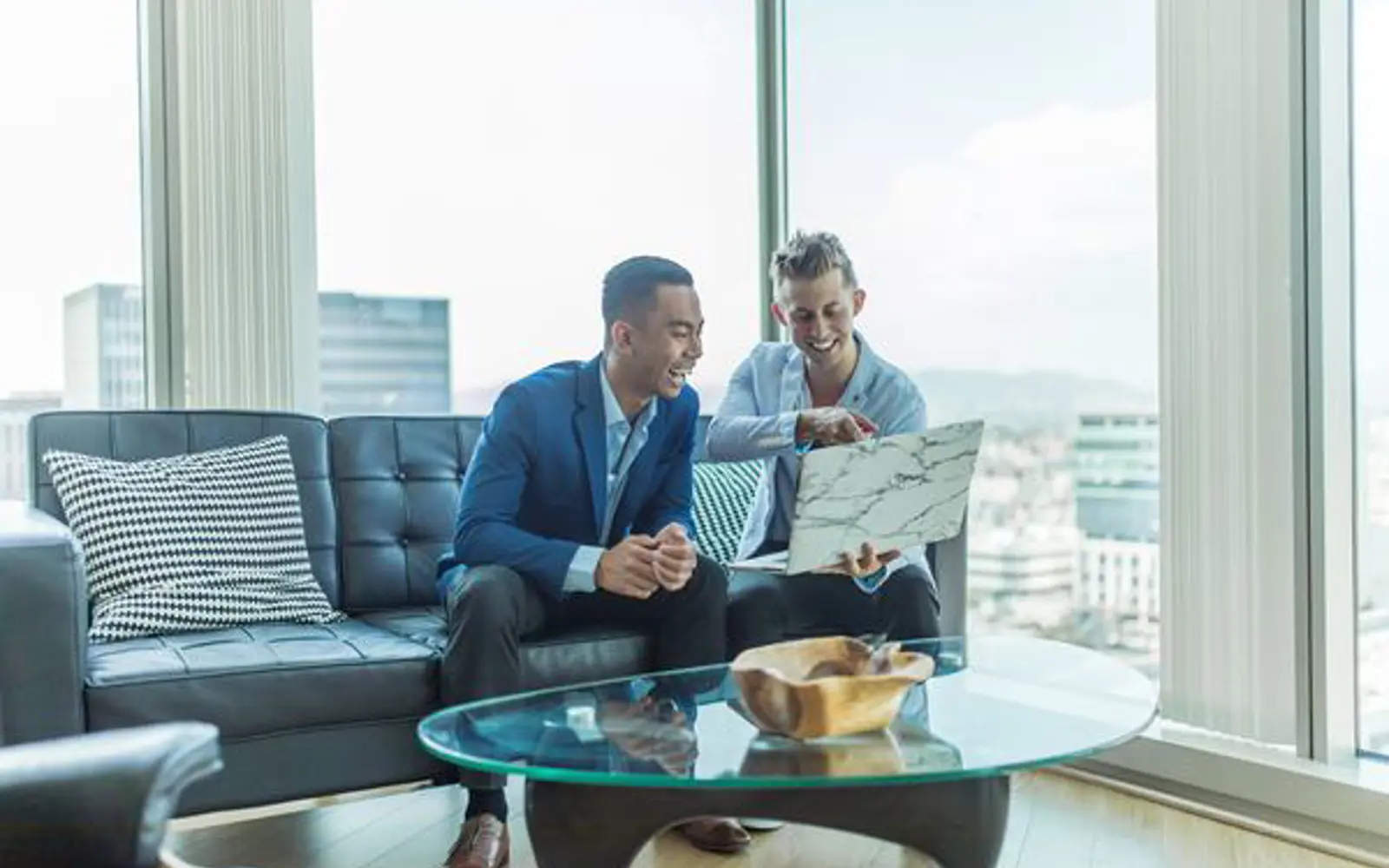 a couple of men sitting on a couch looking at a laptop