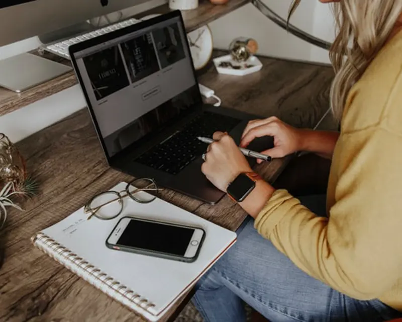 a woman sitting at a desk using a laptop and a phone
