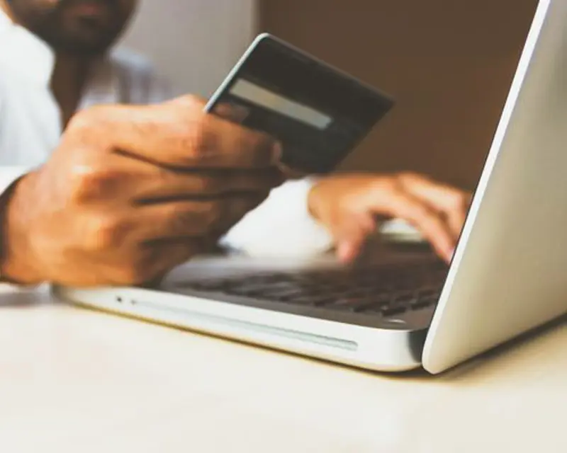 a person holding a credit card and typing on a laptop